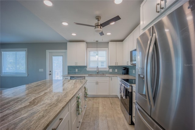 kitchen featuring a sink, stainless steel appliances, ceiling fan, decorative backsplash, and light stone counters