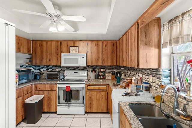 kitchen with a sink, tasteful backsplash, brown cabinetry, and white appliances