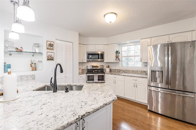 kitchen with light stone countertops, light wood-style floors, white cabinetry, a sink, and stainless steel appliances