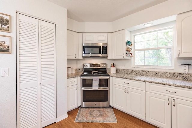 kitchen with white cabinets, light stone countertops, appliances with stainless steel finishes, and light wood-style floors
