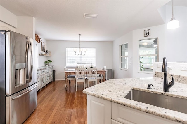 kitchen with a sink, stainless steel fridge with ice dispenser, light wood finished floors, a notable chandelier, and white cabinetry