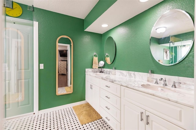 bathroom featuring baseboards, double vanity, a textured wall, and a sink