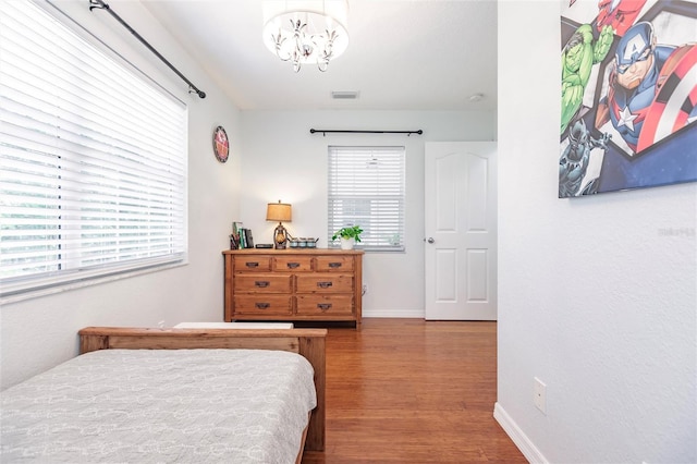 bedroom featuring visible vents, baseboards, wood finished floors, and a chandelier