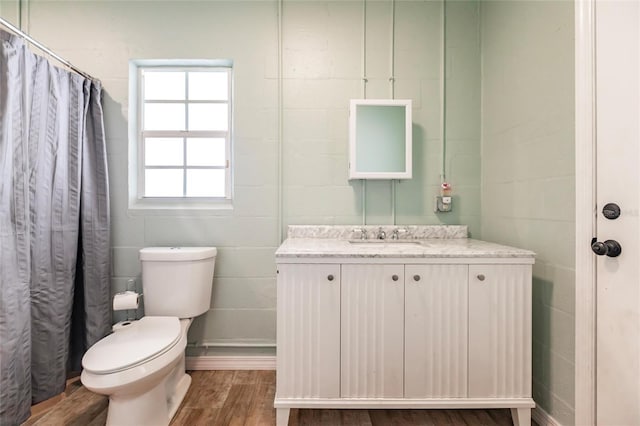 full bathroom with wood finished floors, concrete block wall, vanity, toilet, and a shower with shower curtain