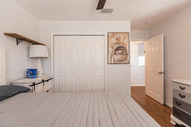 bedroom featuring a ceiling fan, visible vents, wood finished floors, baseboards, and a closet