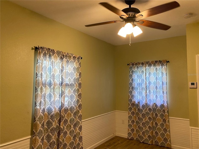 spare room featuring a ceiling fan, wood finished floors, and a wainscoted wall