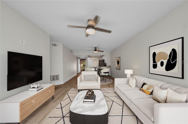 living room with visible vents, baseboards, ceiling fan, and light wood-type flooring