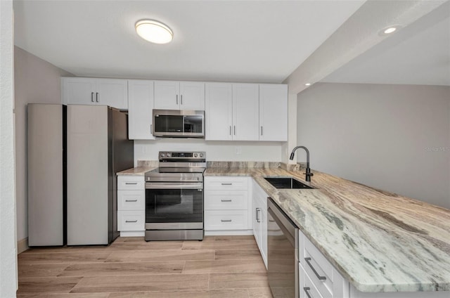 kitchen featuring a sink, appliances with stainless steel finishes, light stone countertops, and a peninsula