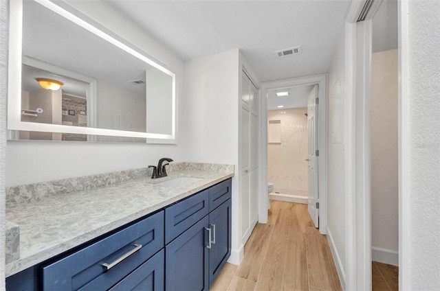 bathroom with vanity, toilet, wood finished floors, and visible vents