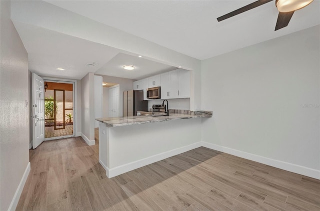 kitchen featuring stainless steel appliances, baseboards, a peninsula, and light wood-type flooring