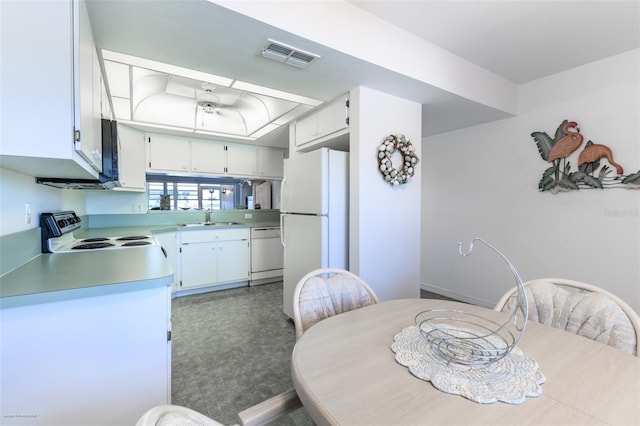 kitchen with a sink, a tray ceiling, visible vents, white appliances, and light countertops