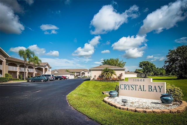 community / neighborhood sign featuring a lawn, a residential view, and uncovered parking