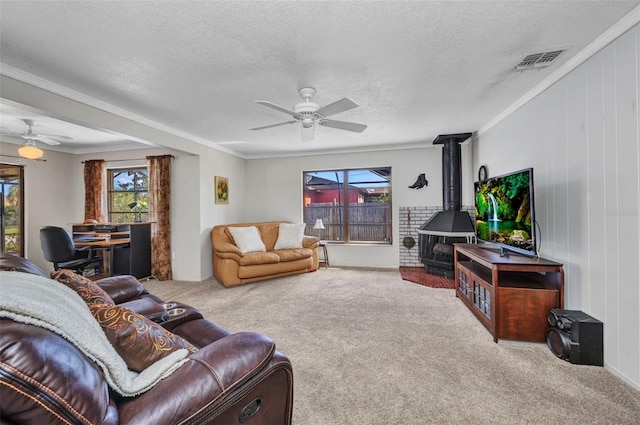 carpeted living room with a ceiling fan, a wealth of natural light, and a wood stove