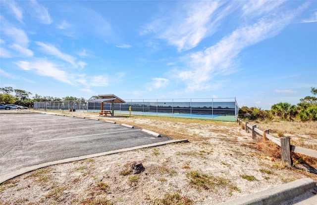 view of home's community with a tennis court, fence, and uncovered parking