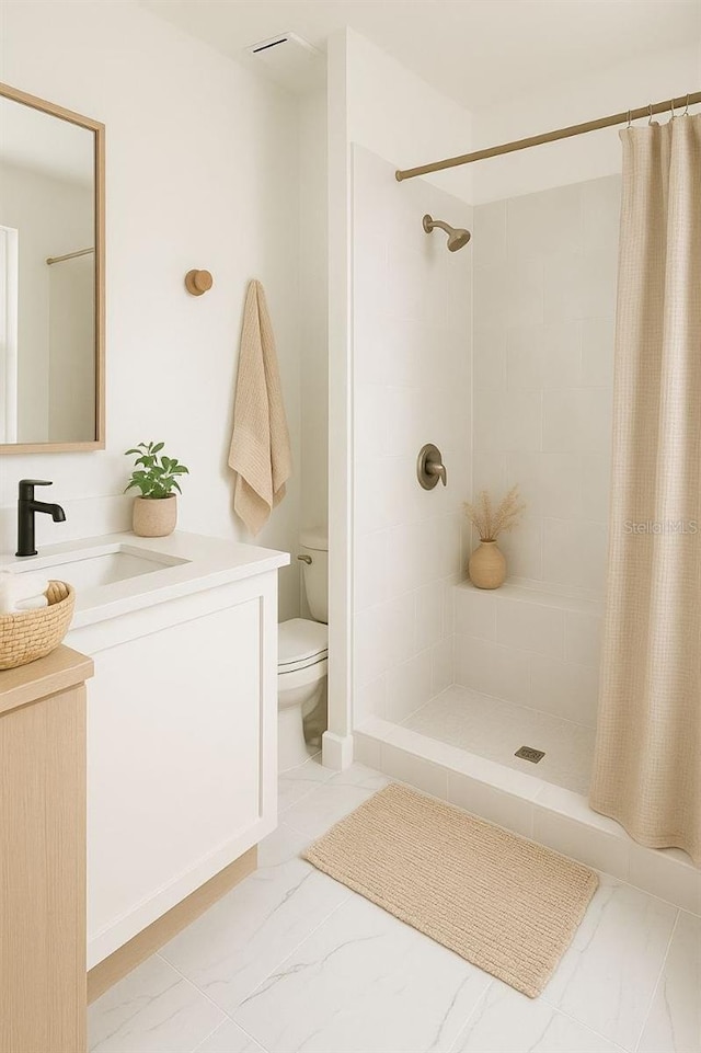 bathroom featuring toilet, tiled shower, marble finish floor, and vanity
