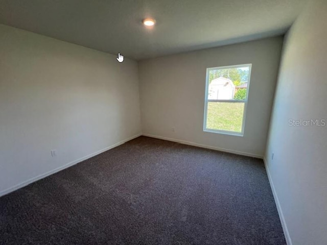 unfurnished room with baseboards and dark carpet