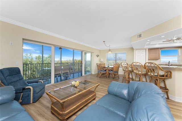 living room with crown molding, visible vents, light wood-style flooring, and baseboards