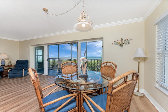 dining area featuring baseboards, crown molding, a water view, and light wood-type flooring