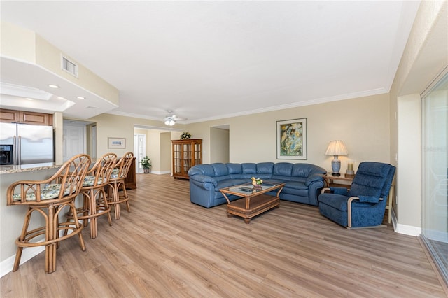 living room with baseboards, ornamental molding, light wood finished floors, and visible vents