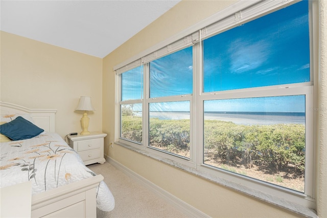 bedroom with light carpet, a water view, and baseboards