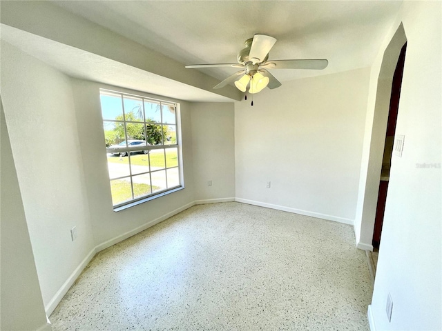 empty room with ceiling fan, baseboards, and arched walkways