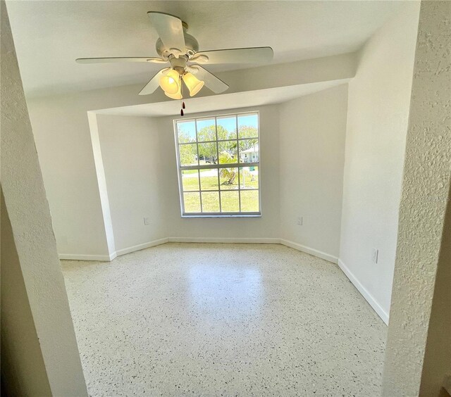 unfurnished room with speckled floor, baseboards, and ceiling fan