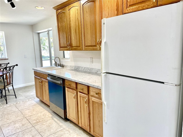 kitchen with a sink, freestanding refrigerator, light tile patterned floors, stainless steel dishwasher, and baseboards