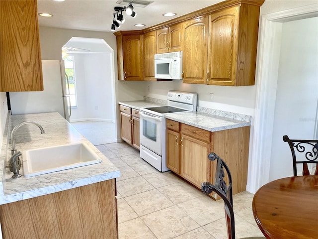 kitchen with a sink, arched walkways, white appliances, light countertops, and light tile patterned flooring