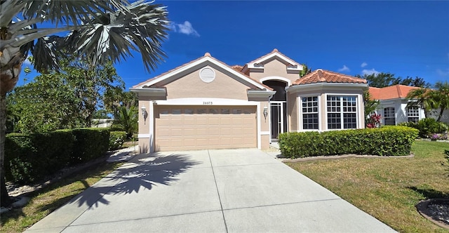 mediterranean / spanish-style home with concrete driveway, a garage, stucco siding, a front lawn, and a tiled roof