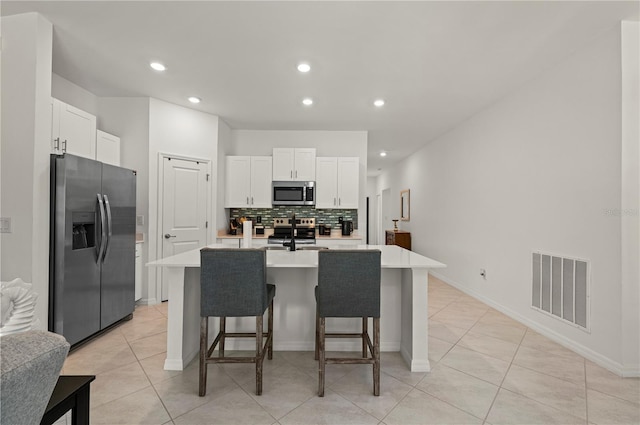 kitchen with stainless steel appliances, light countertops, backsplash, white cabinets, and a breakfast bar area