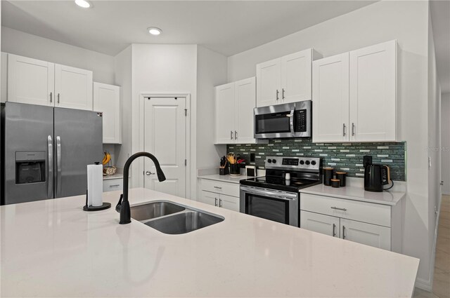kitchen with appliances with stainless steel finishes, a sink, white cabinets, tasteful backsplash, and light countertops