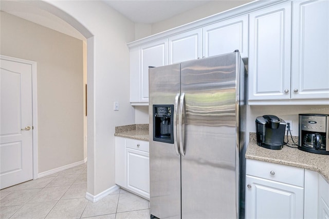 kitchen with stainless steel fridge, arched walkways, light tile patterned floors, white cabinetry, and baseboards