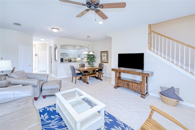 living room featuring light tile patterned flooring, a ceiling fan, arched walkways, stairway, and baseboards