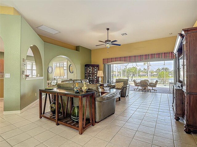 living room featuring a ceiling fan, light tile patterned floors, baseboards, and arched walkways