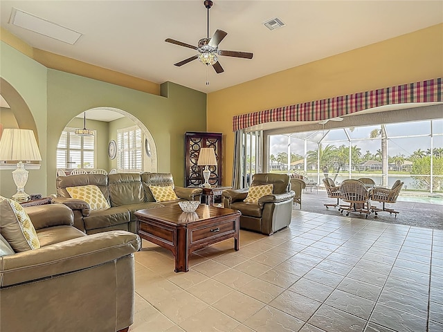 living room featuring a ceiling fan, light tile patterned floors, arched walkways, plenty of natural light, and vaulted ceiling