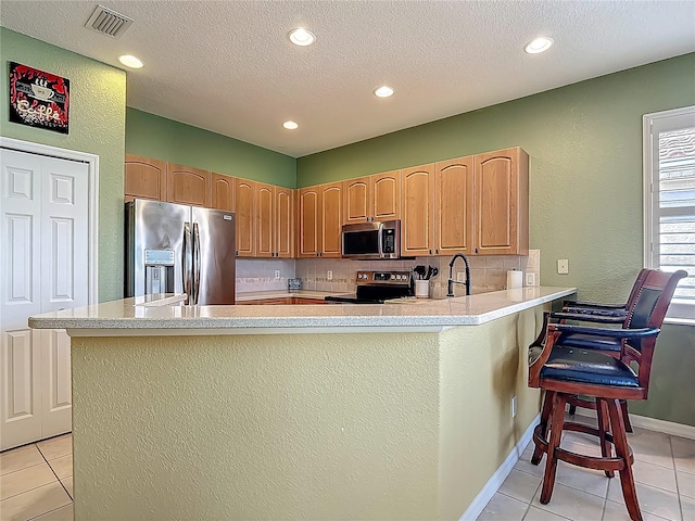 kitchen with stainless steel appliances, light tile patterned floors, a peninsula, light countertops, and a breakfast bar area
