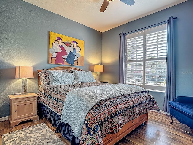 bedroom with multiple windows, wood finished floors, baseboards, and a textured wall