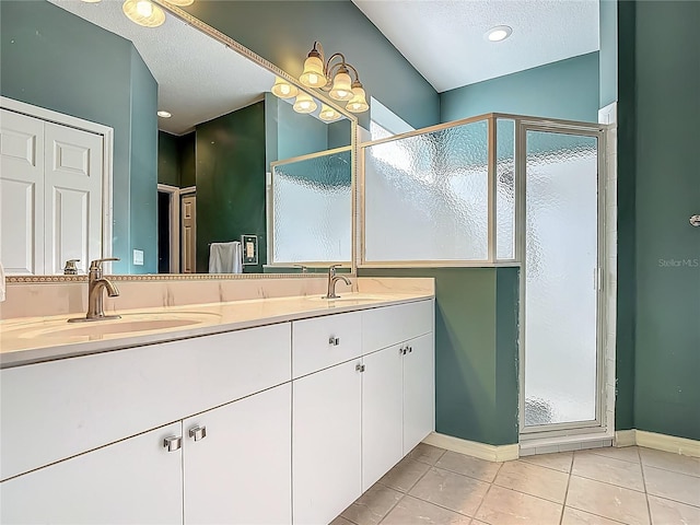 full bath featuring tile patterned flooring, a textured ceiling, a shower stall, double vanity, and baseboards