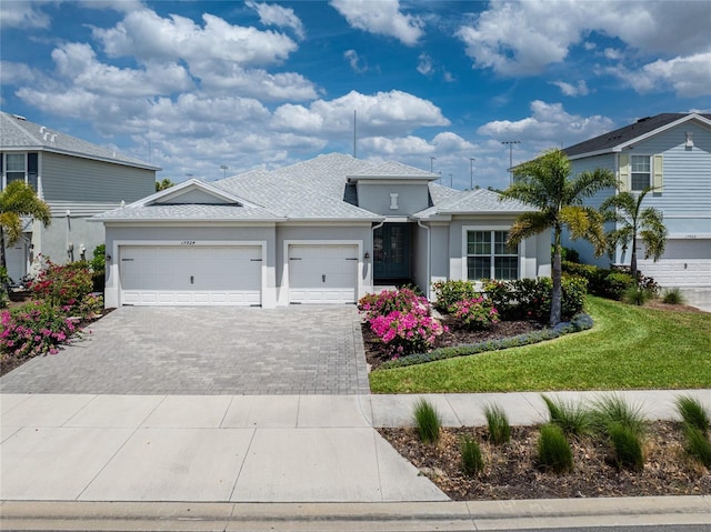 view of front of house with a garage, decorative driveway, stucco siding, roof with shingles, and a front yard