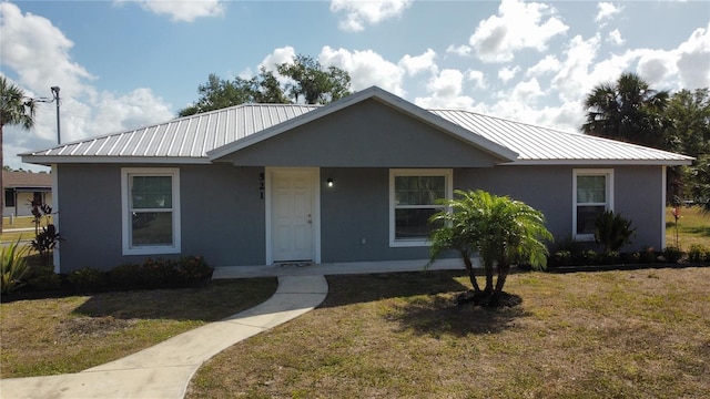 view of front facade with a front lawn, stucco siding, and metal roof