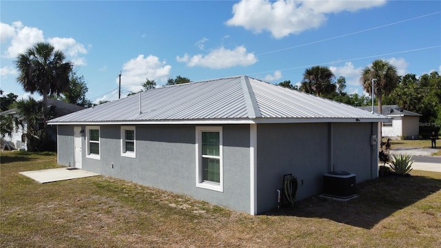 view of side of home with a yard, stucco siding, central AC unit, and metal roof