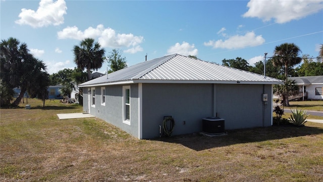 rear view of property with a yard, metal roof, stucco siding, and central AC