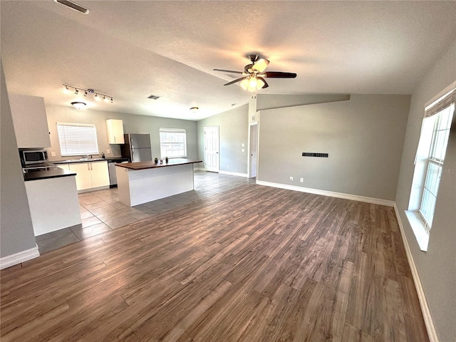 unfurnished living room featuring a textured ceiling, baseboards, a ceiling fan, and dark wood finished floors