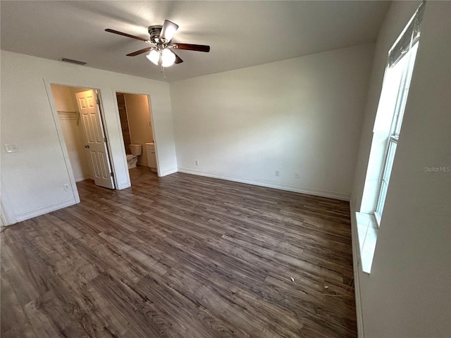 unfurnished bedroom featuring a closet, a walk in closet, dark wood-type flooring, baseboards, and visible vents