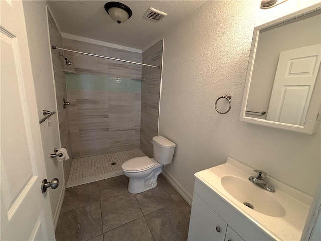 bathroom with toilet, tiled shower, visible vents, tile patterned flooring, and vanity