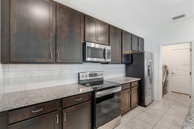1443 SW 1st St, Cape Coral, FL 33991 - kitchen with stainless steel appliances, washing machine and clothes dryer, dark brown cabinets, light tile patterned floors, and backsplash
