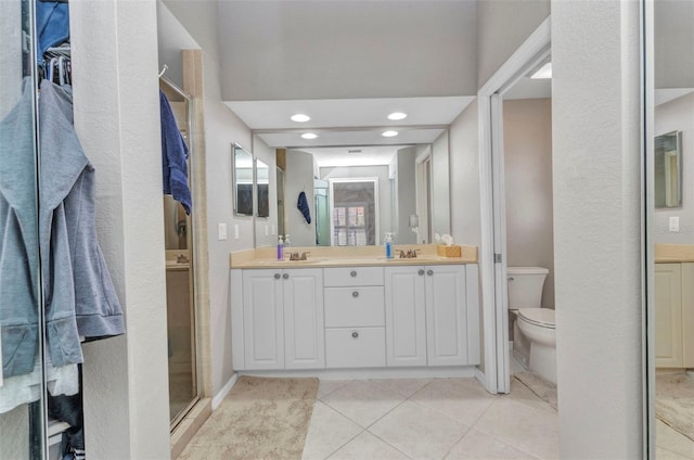 bathroom featuring toilet, a sink, a shower stall, tile patterned floors, and double vanity