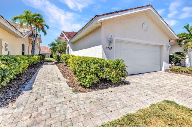 view of side of property with stucco siding, a tile roof, a garage, and decorative driveway