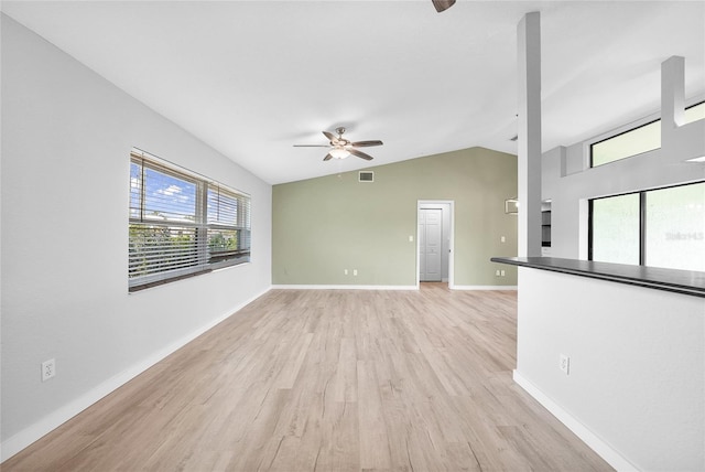 unfurnished living room featuring a ceiling fan, vaulted ceiling, light wood finished floors, plenty of natural light, and baseboards