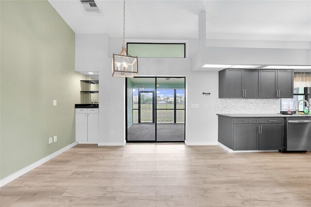 kitchen featuring stainless steel dishwasher, a chandelier, light wood finished floors, and tasteful backsplash
